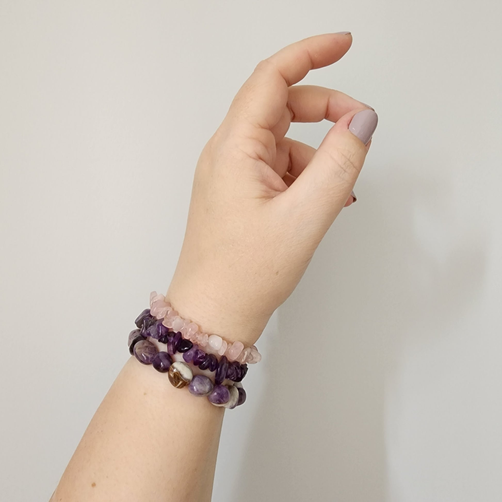 Hand and arm with multiple gemstone bracelets- rose quartz, amethyst and agate.